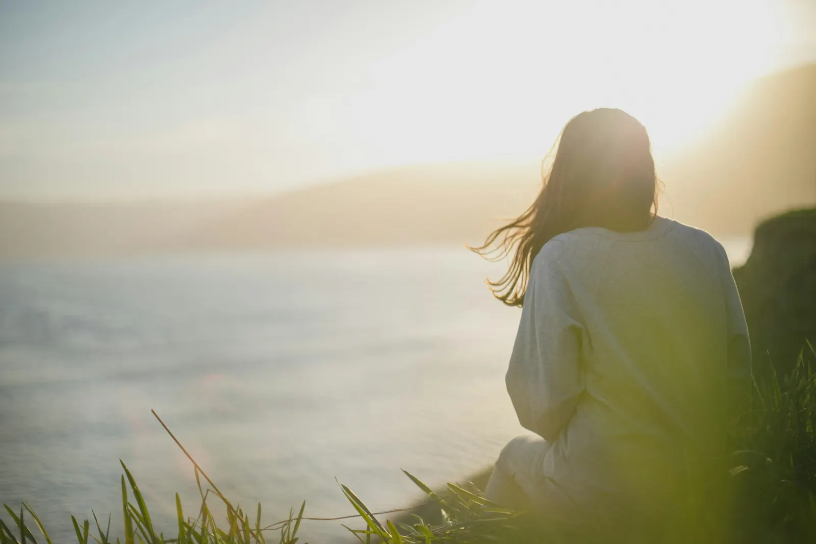 Mujer sentada frente al mar al amanecer